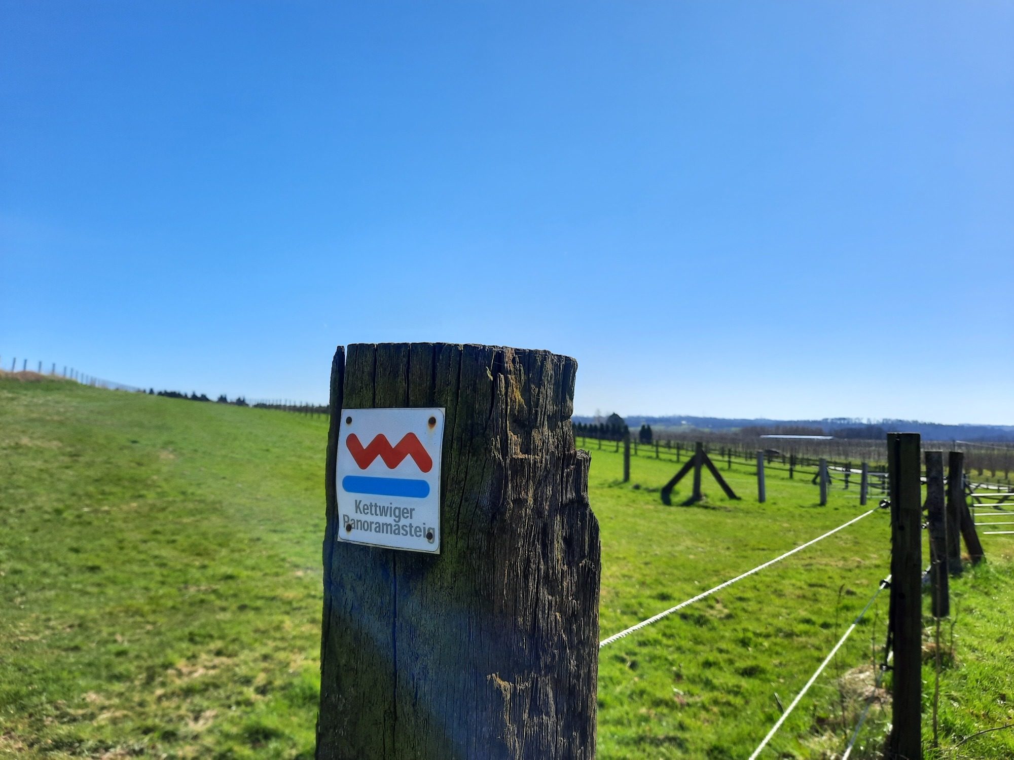 Zaun auf einer Weide und dem Schild mit der Aufschrift Kettwiger Panoramasteig